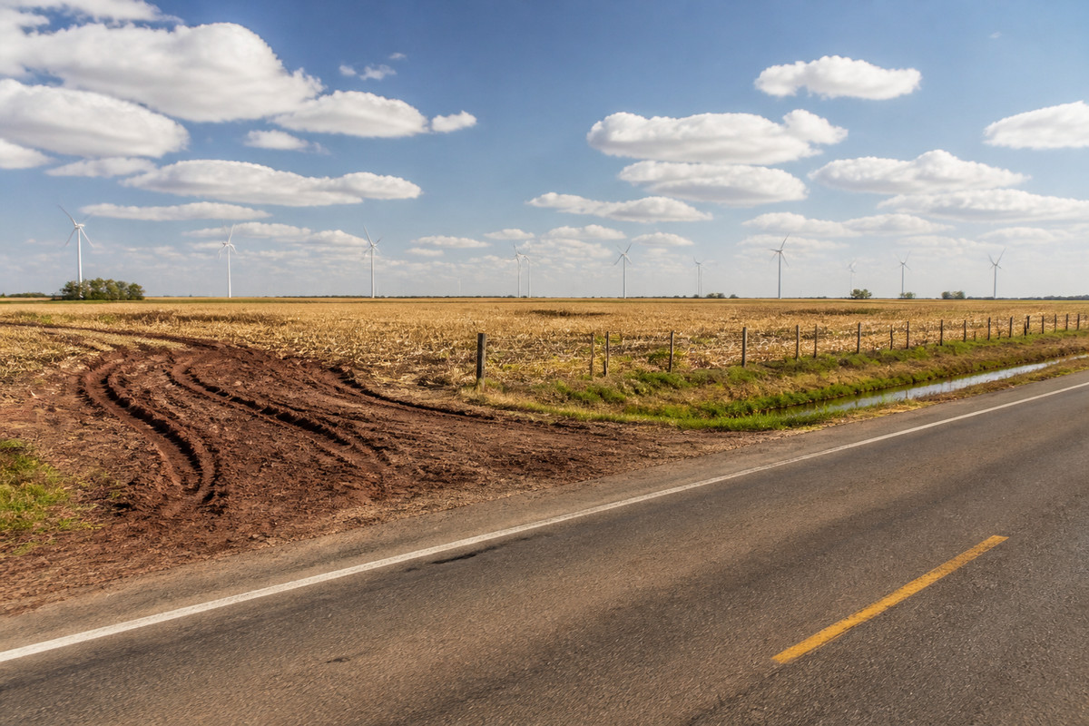 Open Thumb farmland in Huron County with a wind turbine line and a clay field entrance off a two lane road
